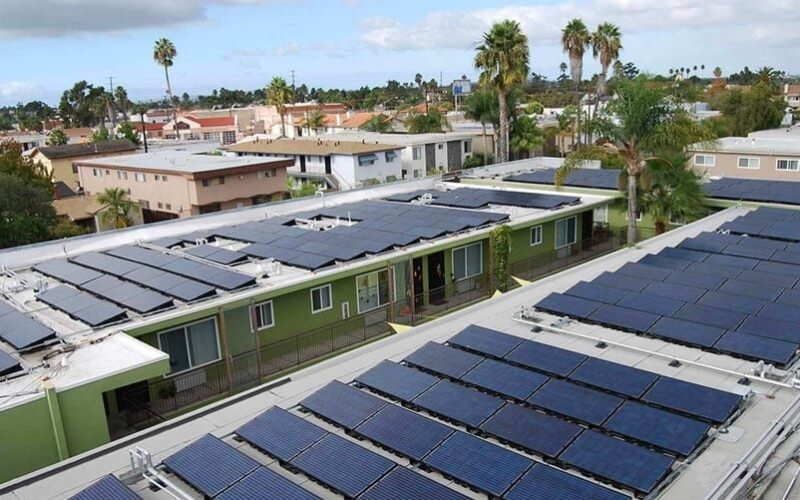 Apartment complex rooftops covered with solar panels among palm trees