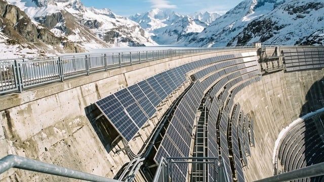 Solar panels installed on a concrete alpine dam amid snowy mountains